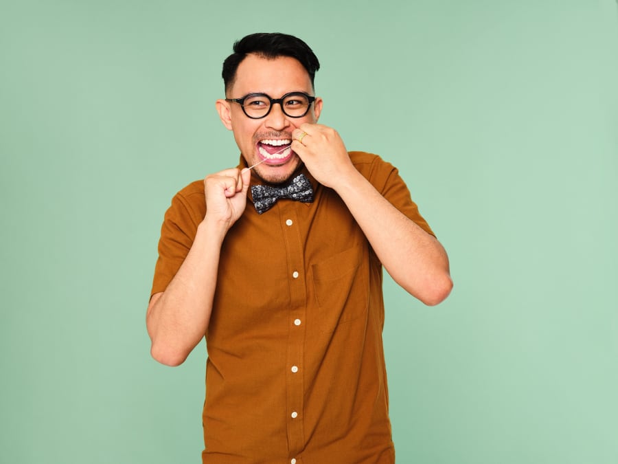 Happy man wearing a bow tie and glasses, flossing his teeth.