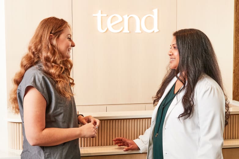 Two professionals in a Tend Dental reception area chatting.