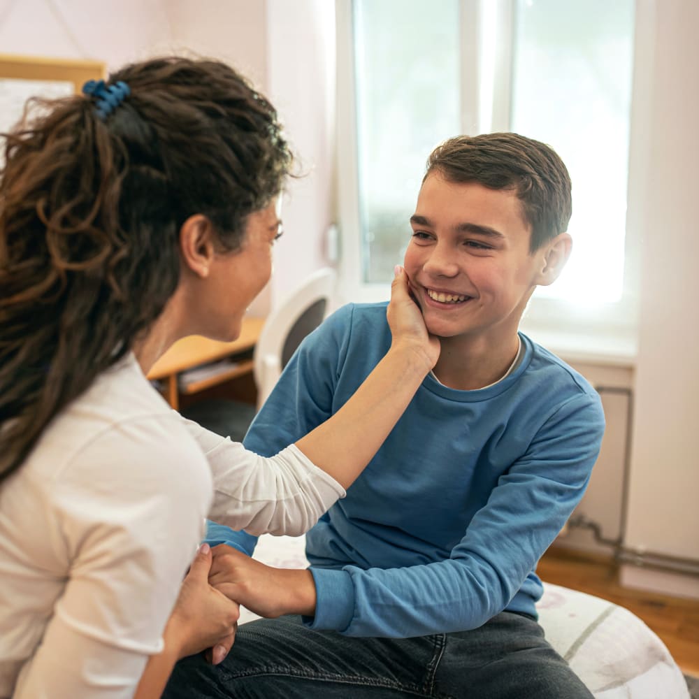 A woman looking at a smiling boy while holding his face in her hand.